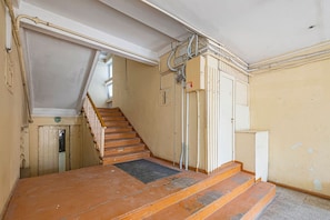 Una scala conduce a un pianerottolo con ringhiera, una porta e cavi elettrici a vista.