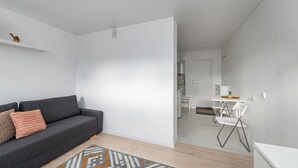 Een moderne woonkamer met een grijze bank, een kamerbreed tapijt met een patroon, en een witte deur die leidt naar een badkamer.