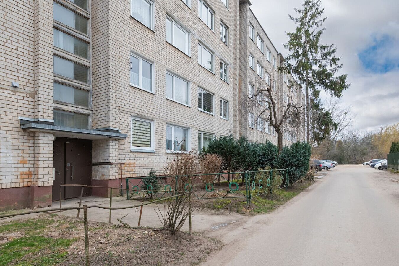 Un immeuble résidentiel à plusieurs étages, doté d’une façade en briques, de nombreuses fenêtres et d’une allée d’accès fermée par un portail.