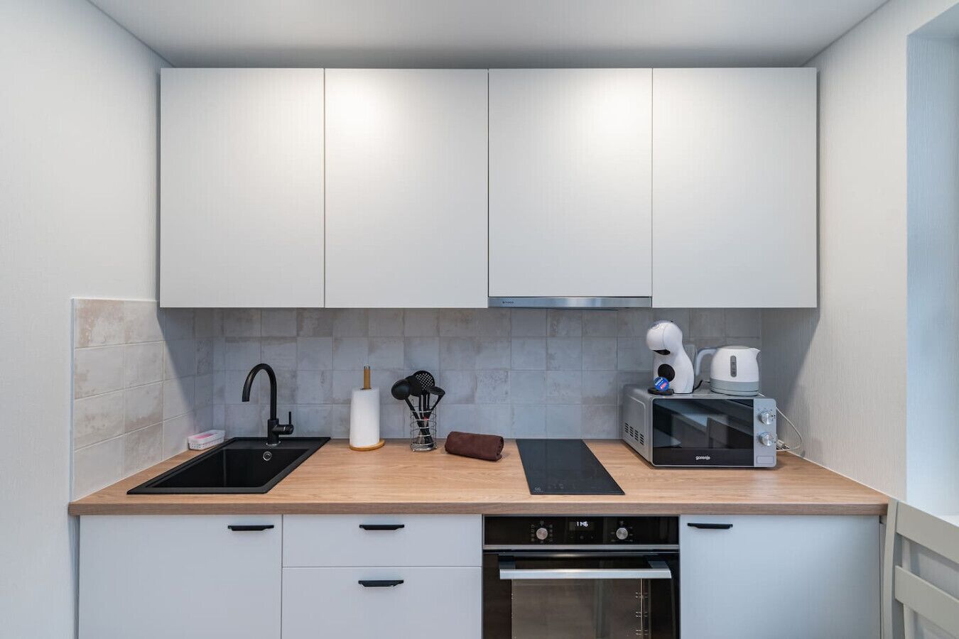 A modern kitchen with white cabinets, a black sink, a built-in oven, and a microwave.