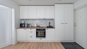 A compact kitchen with white cabinets, a microwave, toaster, kettle, and a sink.