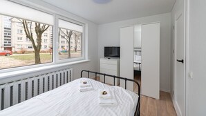 A bedroom with a bed, a dresser, a TV, and a view of a building outside.