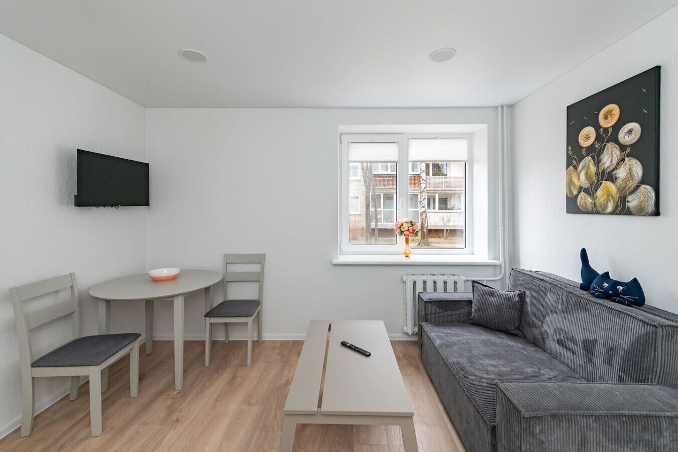 Ein modernes Wohnzimmer mit einer Couch, einem Esstisch, Stühlen, einem Fernseher und einem Fenster mit Blick auf Gebäude.
