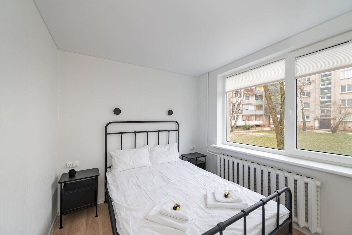 Un dormitorio con cama, mesita de noche, ventana con persianas y radiador.