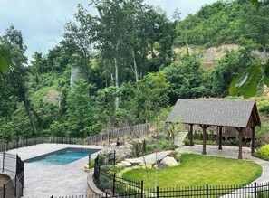 A swimming pool surrounded by a fence, a gazebo, and a well-maintained lawn.