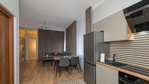 A modern kitchen with a built-in oven, a dining area with a table and chairs, and a separate dining room with a sofa and curtains.