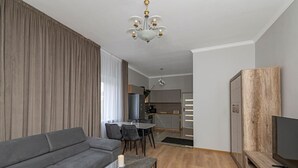 A modern living room with a grey sofa, a coffee table, a TV stand, and a dining area with a table and chairs.