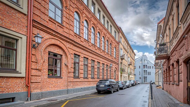 A narrow street lined with red brick buildings, parked cars, and a clear sky.