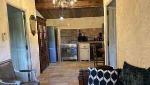 A cozy living room with a sofa and a patterned pillow, a wooden ceiling, and a kitchen in the background. - "A Figa" Authentic stay in U Sirenu (SARTENE)