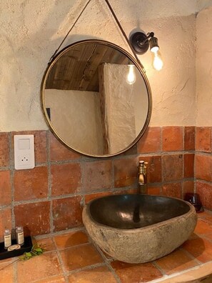Une salle de bain avec un miroir rond, un lavabo en pierre et un luminaire.