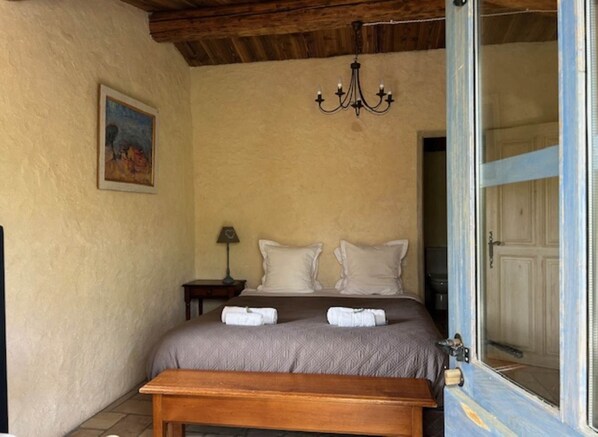 Une chambre à coucher avec un lit, une table de chevet avec une lampe, un banc, un tableau au mur et un lustre.