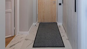 Un pasillo con una puerta de madera, un felpudo negro y un suelo con diseño de mármol.