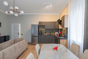 Une cuisine moderne équipée d’un réfrigérateur, d’un four à micro-ondes et d’une cuisinière, un coin repas avec une table et des chaises, et un salon avec un canapé.