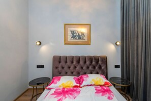 Une chambre à coucher avec une tête de lit capitonnée, un lit recouvert d’une literie à motifs floraux, deux tables de chevet et un tableau encadré accroché au mur.