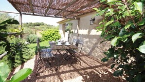 An outdoor patio with a table and chairs, a pergola providing shade, and a view of the surrounding garden and hills. - "U Pireddu" Relaxation and comfort at U Sirenu (SARTENE)