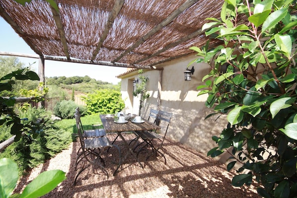 Une terrasse extérieure avec une table et des chaises, une pergola offrant de l’ombre et une vue sur le jardin et les collines environnants.