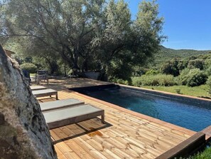 Una terraza de madera con piscina, rodeada de árboles y un paisaje montañoso.