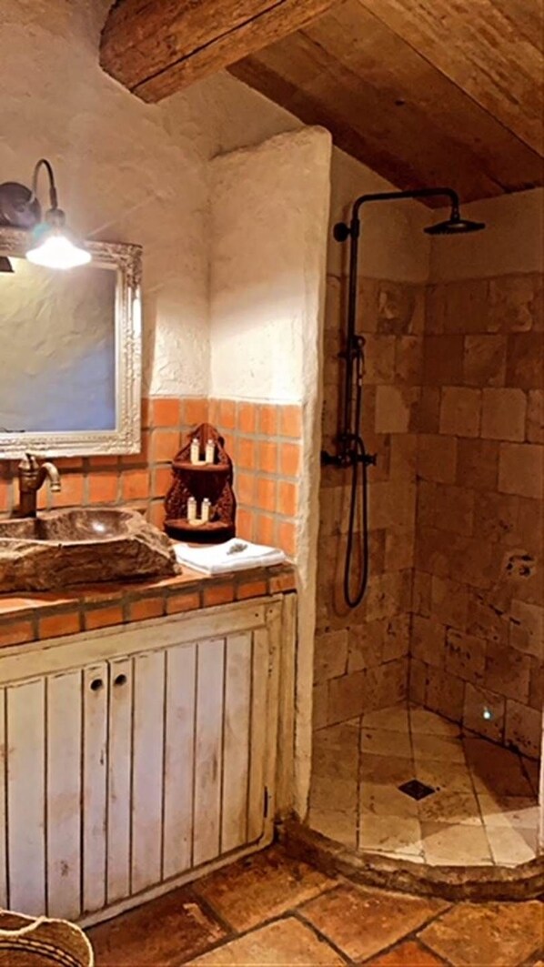 Een rustieke badkamer met een stenen douche, een houten wastafelmeubel en een betegelde spatwand.