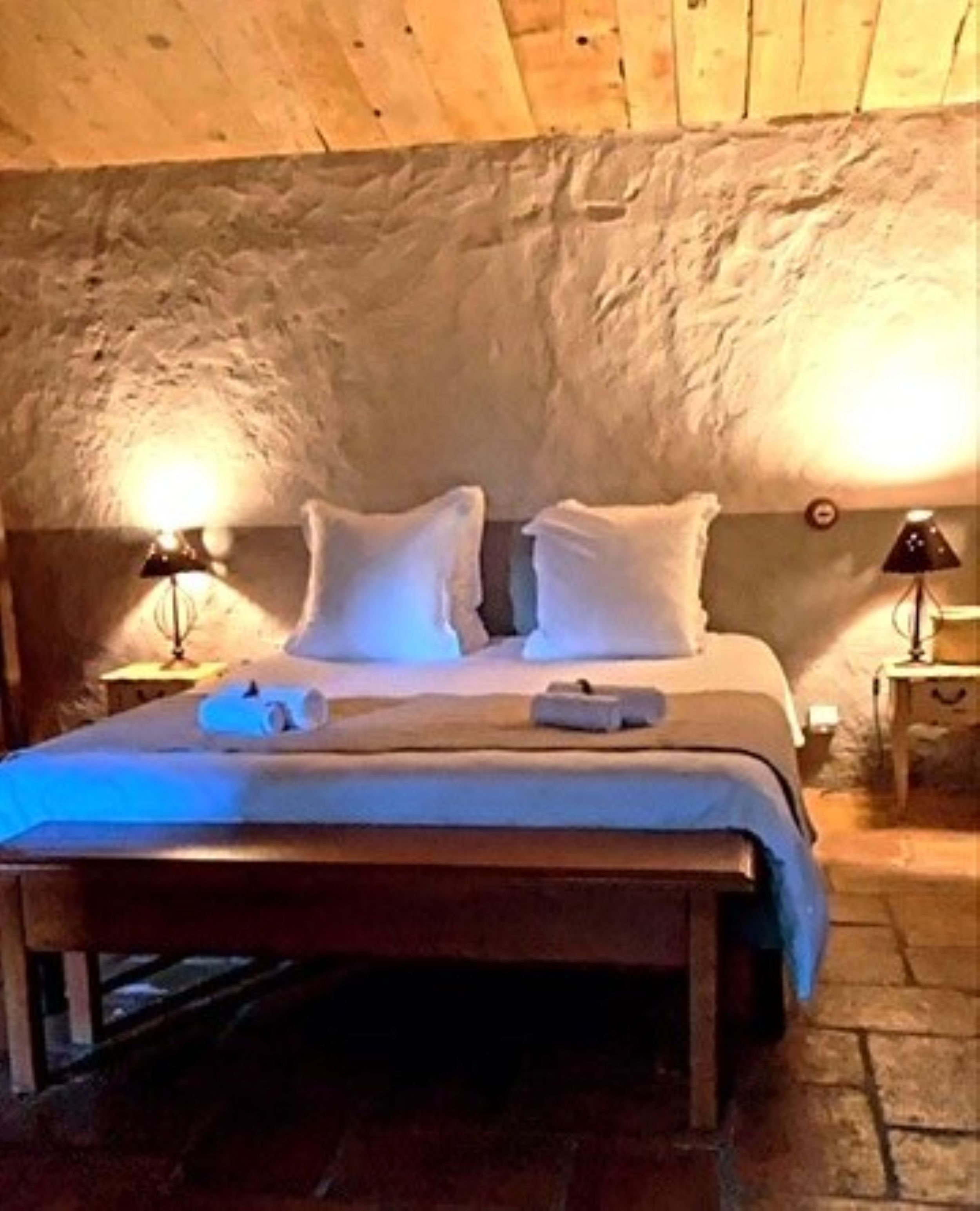 Ein Schlafzimmer mit Holzbalkendecke, einem Bett mit weißer Bettwäsche, zwei Nachttischlampen und einem Nachttisch.