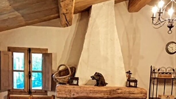 Una habitación rústica con chimenea de piedra, vigas de madera, un banco y una mesa de comedor.
