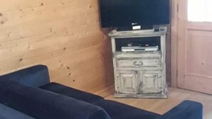 Une pièce avec un canapé bleu, un téléviseur posé sur un meuble en bois et un mur en bois orné d’une horloge.