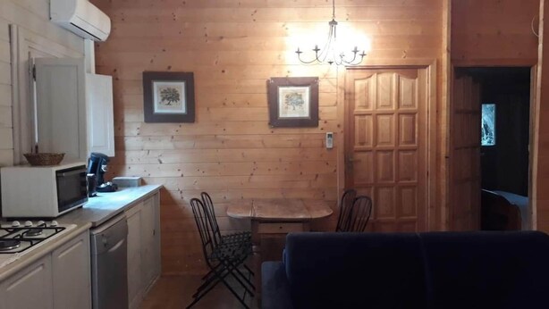Une cuisine compacte équipée d’une cuisinière à gaz, d’un four à micro-ondes et d’une petite table à manger avec des chaises. Deux tableaux encadrés ornent le mur et un lustre est suspendu au-dessus de la table.