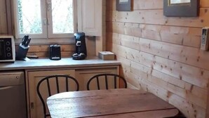 Un intérieur en bois comprenant une table et des chaises, un coin cuisine avec des appareils électroménagers, et des tableaux encadrés accrochés au mur.