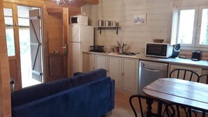 Une cuisine compacte équipée d’un four à micro-ondes, d’une cuisinière et d’un évier. On y trouve un canapé bleu et une table en bois avec des chaises.