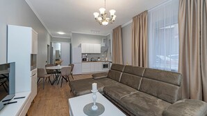 A modern living room with a sofa, a dining area, a kitchen, and a TV. - The Comfort Ap 3 by Polo Apartments (Kaunas)