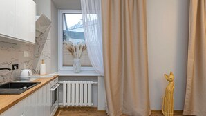 A modern kitchen with white cabinets, a wooden countertop, a window with a view, a radiator, and a decorative cat sculpture. - The Comfort Ap 3 by Polo Apartments (Kaunas)