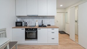 A modern kitchen with white cabinetry, a built-in oven, a microwave, and a coffee machine. - Studio Ap Flora by Polo Apartments (Kaunas)