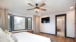 Ein Schlafzimmer mit Bett, Deckenventilator, Fernseher und einem durchgehenden Türspalt sichtbarem Badezimmer.