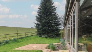 A stone patio with a large evergreen tree in the background. - The Barn (Bridgwater)