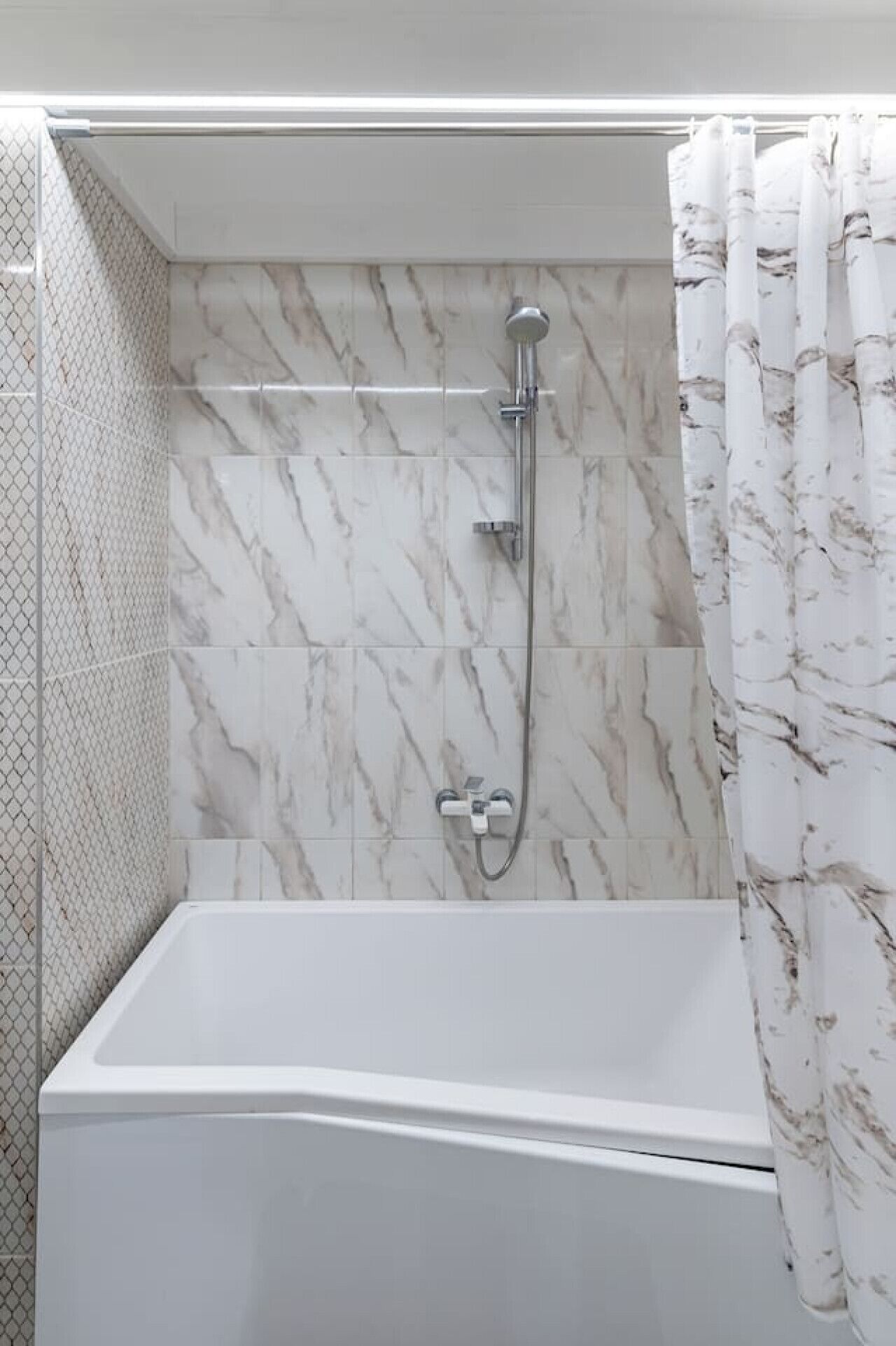Een badkamer met een wit bad, een douche met een handdouche en een wand met een marmerpatroon.