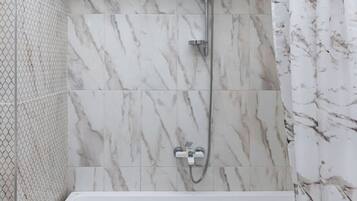 Een badkamer met een wit bad, een douche met een handdouche en een wand met een marmerpatroon.