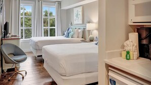 Habitación de hotel con dos camas, un escritorio con silla, un ventilador de techo y vistas al exterior.