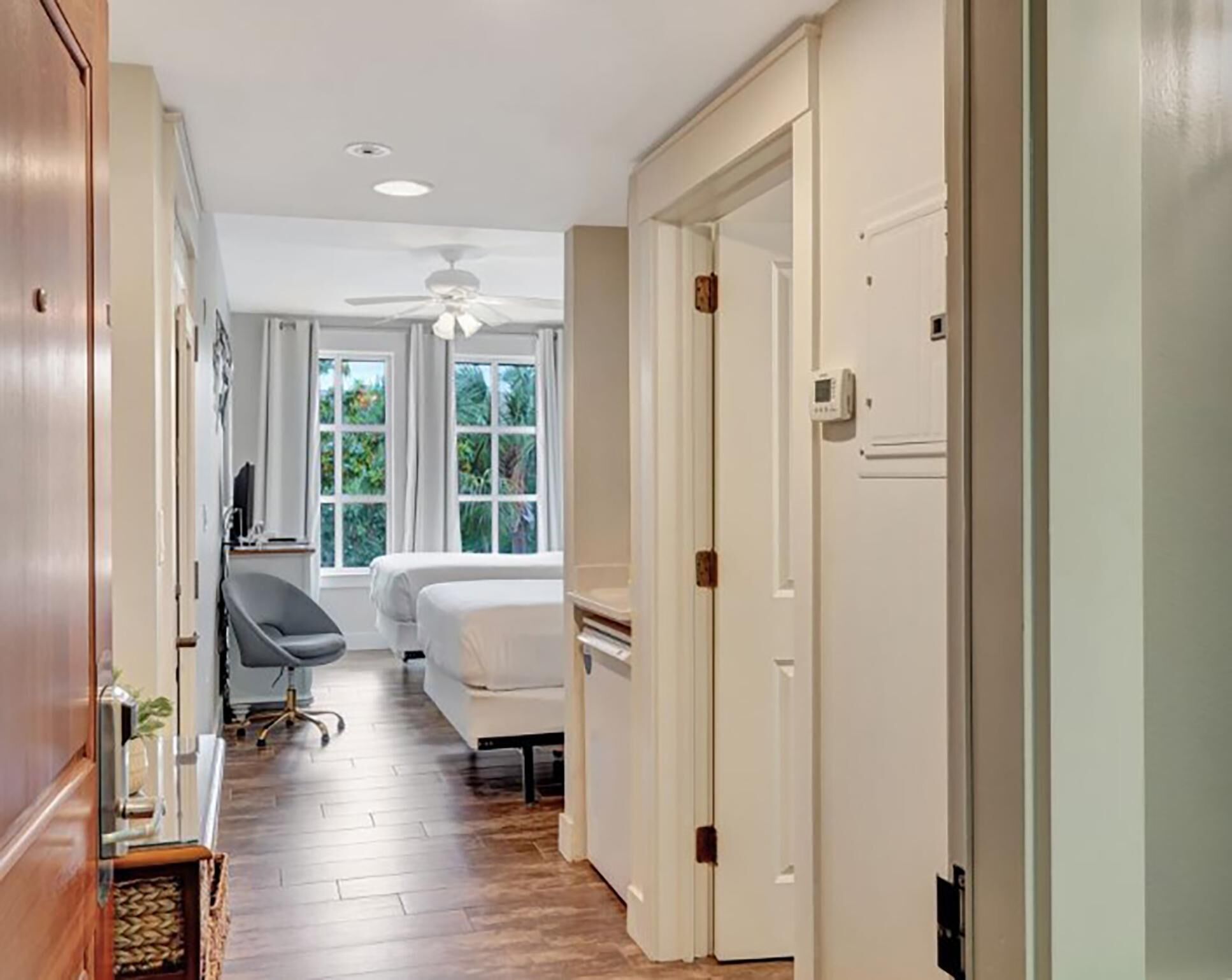 Une chambre d’hôtel avec un plancher en bois, un lit, un bureau, une chaise et un ventilateur de plafond.