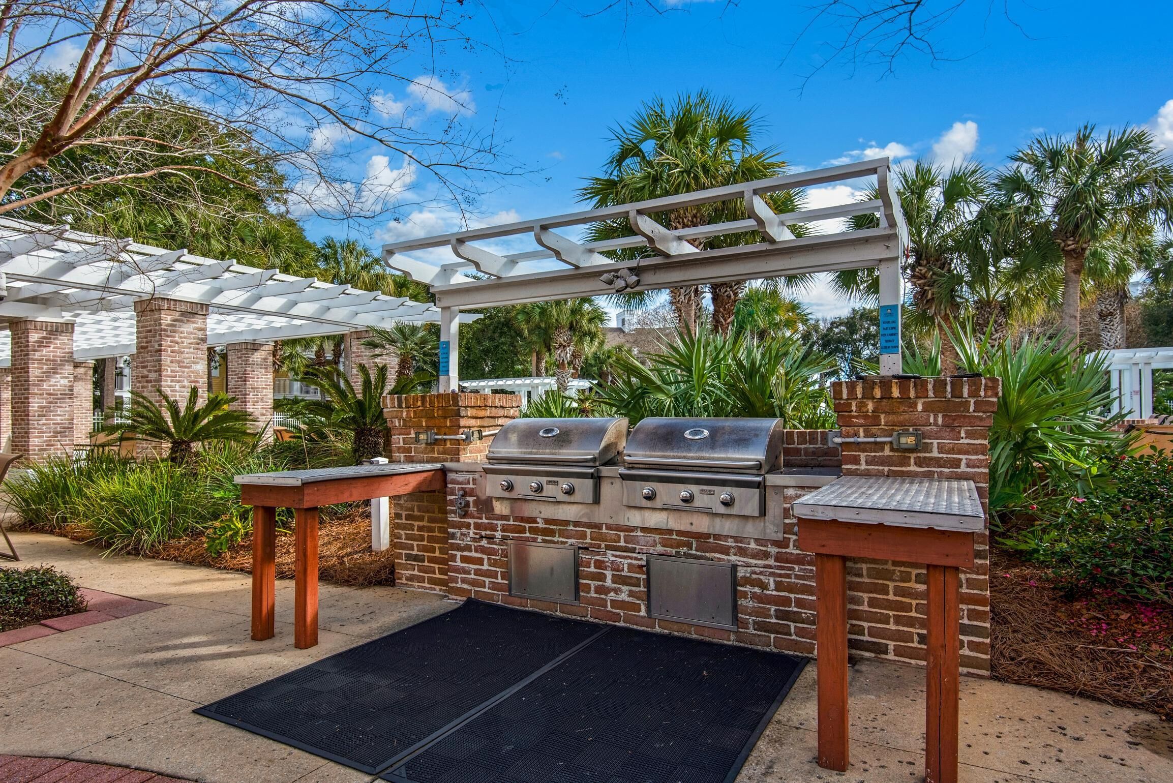 An outdoor barbecue area with a brick grill, two side tables, and a pergola.