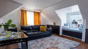 Een modern loft appartement met een eethoek, een zwarte leren bank, een groot raam met gordijnen en uitzicht op de stad.