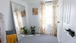 Een kamer met een grote spiegel, een bloempot, een radiator en een raam met bloemen gordijnen.