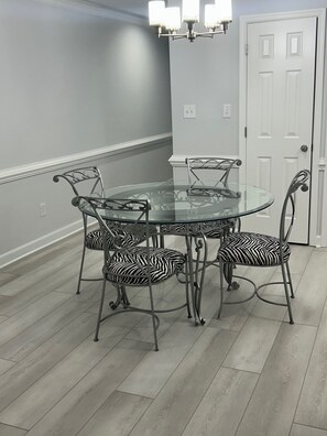 Un coin repas avec une table en verre entourée de chaises à motifs zébrés, une porte blanche et un lustre.