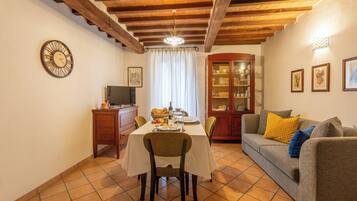 Un coin repas avec une table dressée pour deux personnes, un canapé, un meuble et une horloge au mur.