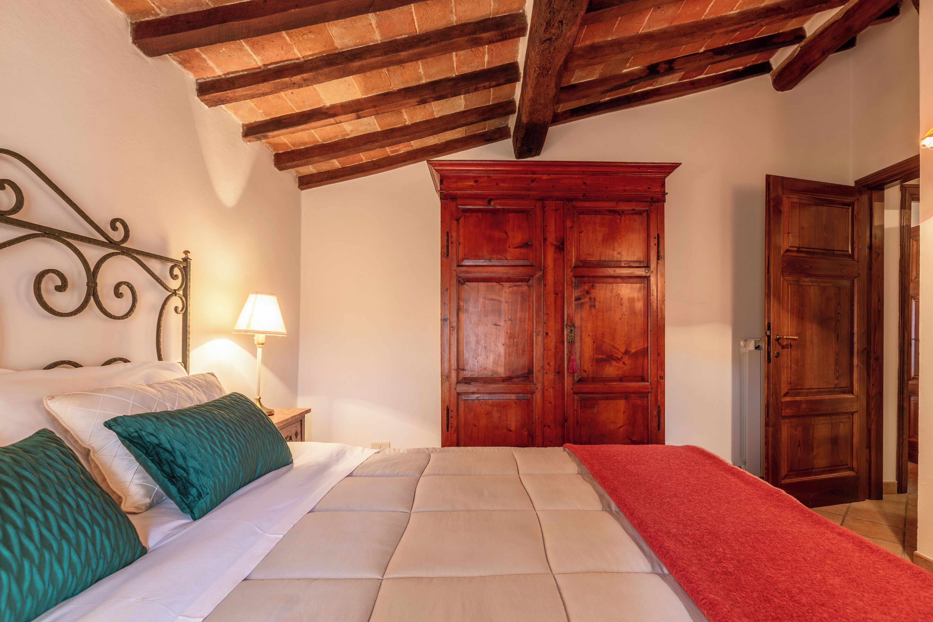 Een slaapkamer met een bed, een houten garderobe en een rode plaid.
