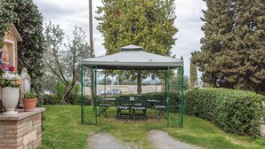 En pavillon med et bord og stole, omgivet af grøn vegetation og en murstensmur.