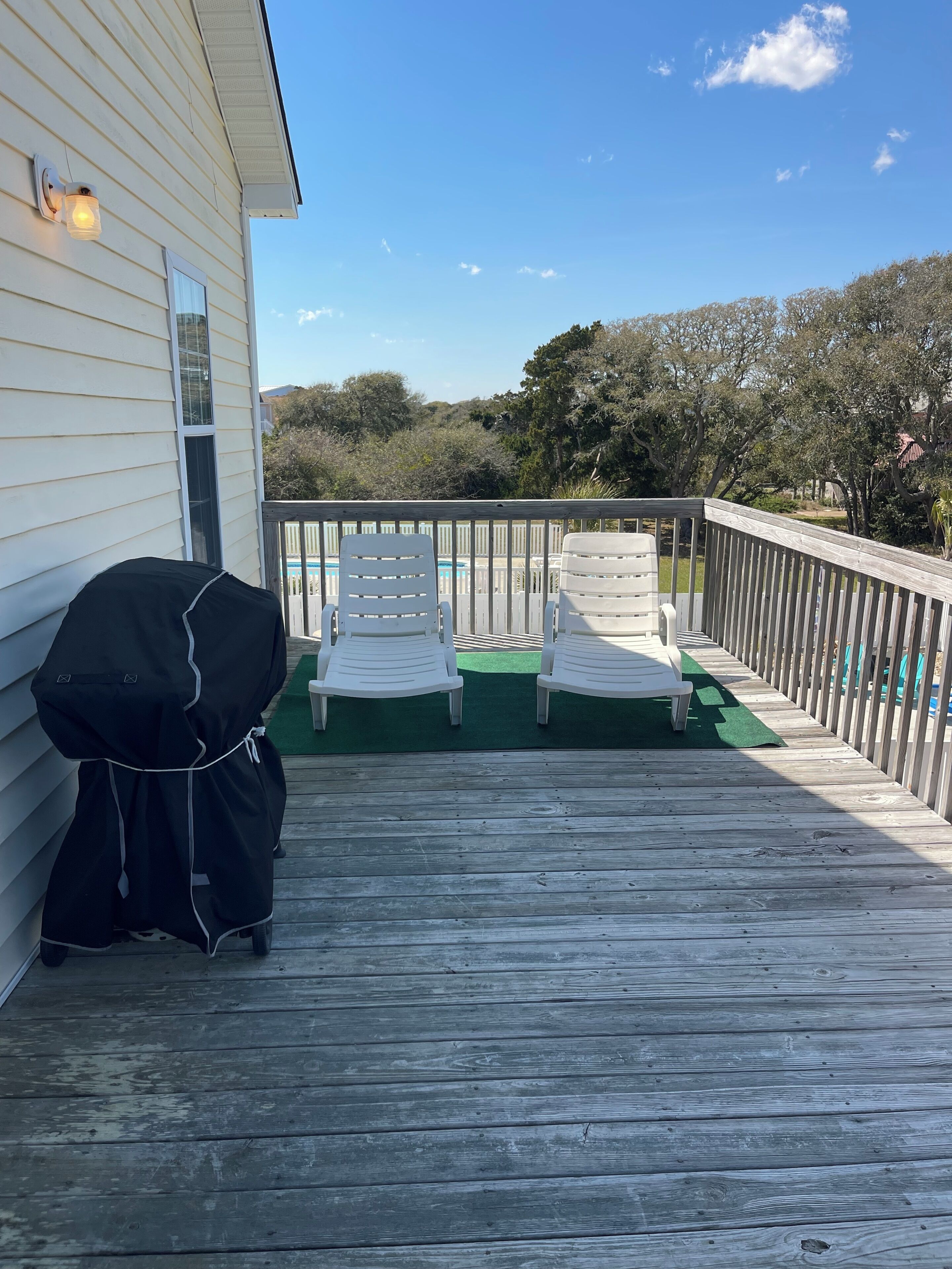Une terrasse en bois avec deux chaises longues blanches et un barbecue.