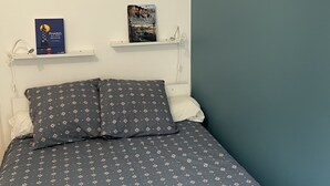 Un dormitorio con cama, almohadas, una mesita de noche y dos libros en estanterías.