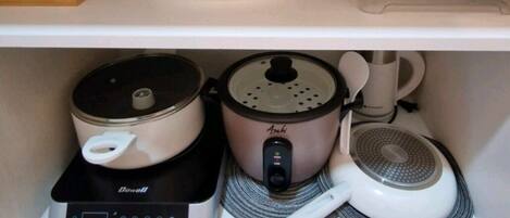 A kitchen area with a countertop, a rice cooker, a coffee maker, and a drawer with utensils.