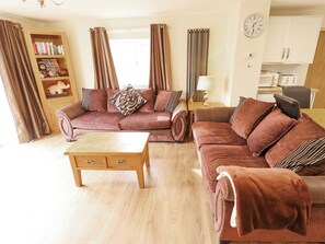 A living room with a brown sofa set, a wooden coffee table, a bookshelf, and a kitchen area in the background. - Willow Cottage (Barrow upon Humber)