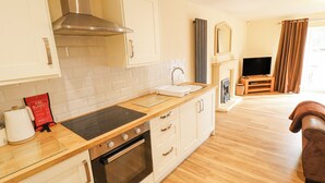 Eine moderne Küche mit Herd, Backofen und weißen Schränken. Auf der Arbeitsfläche liegt eine Branddecke, und im Wohnbereich befindet sich ein Fernseher.