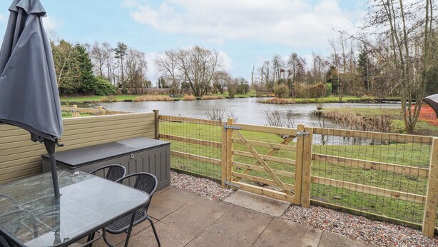 Eine Terrasse mit Tisch und Stühlen, einem Sonnenschirm und Blick auf einen Fluss und einen Park.
